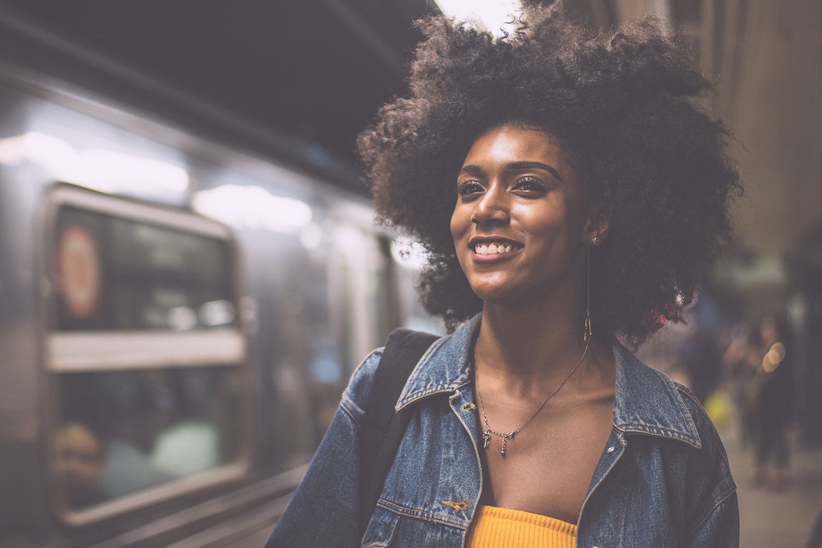 Black women smiling with an afro at the train station.